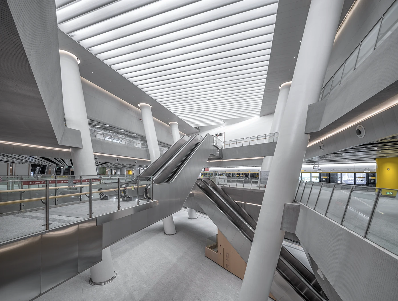 Gangxia North hub: escalators crossing between levels under a ribbed ceiling